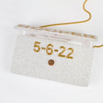 "Custom Mrs (Last Name)" beaded bridal clutch, intricately handmade for an elegant touch on the wedding day. Sized at 9.5in x 5in x 3in with an option for a gold or silver chain. Each bridal clutch boasts a unique character, highlighting the beauty of handcrafted items. Can be personalized with a custom date inside. An exquisite addition to any bridal ensemble or a thoughtful gift for soon-to-be brides.