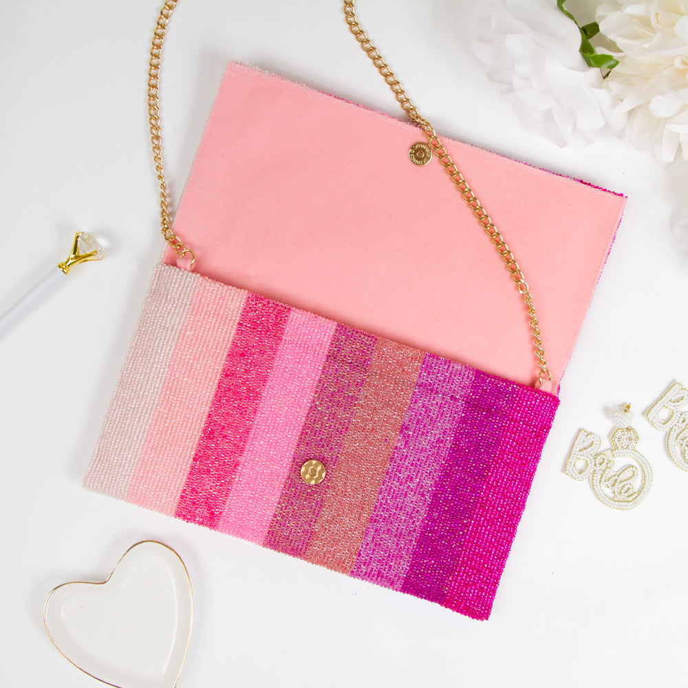 Exquisite Personalized Pink Ombre Clutch Bag, masterfully handcrafted for wedding occasions. Measuring 9.5 inches in length and 6 inches in breadth, this clutch features a gradient of pink hues, accented with white text beading. Complete with a gold or silver chain and plush velvet interior, it can be personalized with a date inside. A perfect blend of elegance and functionality, it's a distinctive accessory that adds a touch of sophistication to bridal attire.
