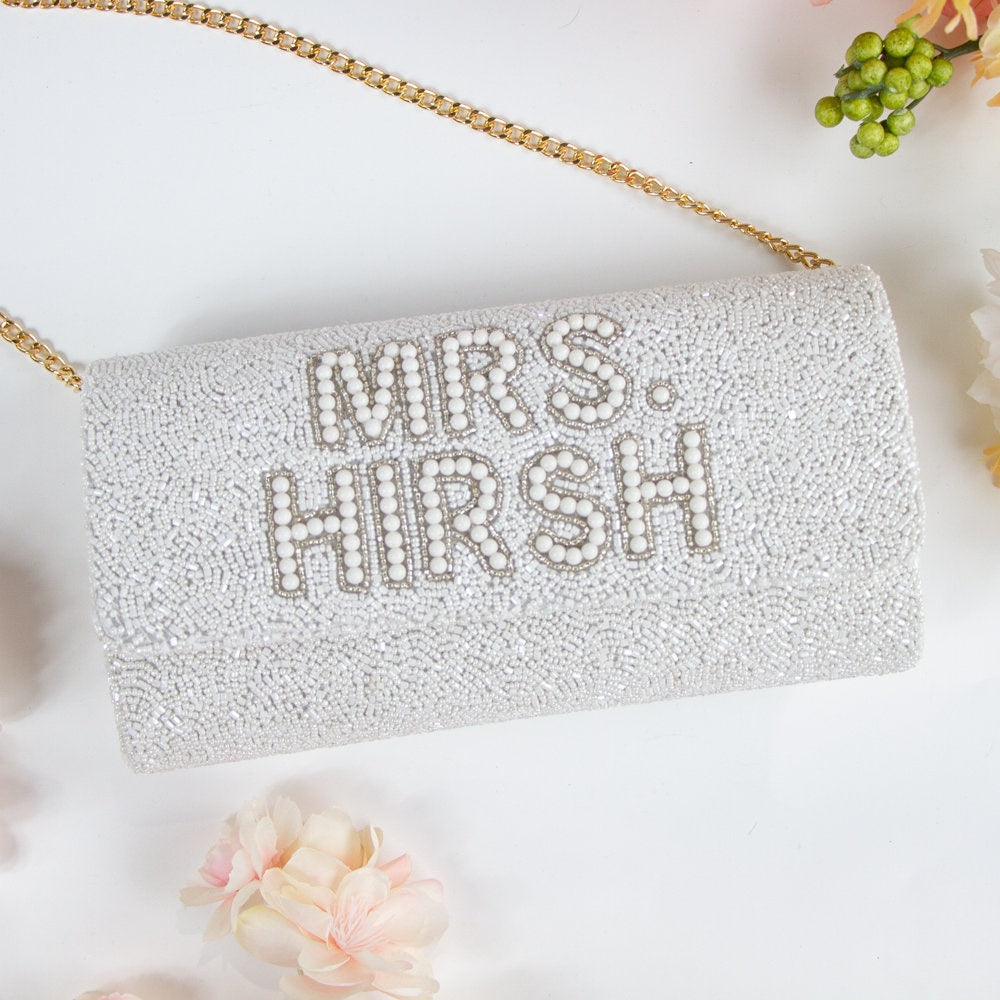 "Handmade pearl beaded bridal clutch with an intricate pattern, perfect for wedding day essentials. Comes with a gold or silver chain, sized at 9.5in x 5in x 3in. Features the option for a custom date inside. Unique design variations make each bridal clutch one-of-a-kind."