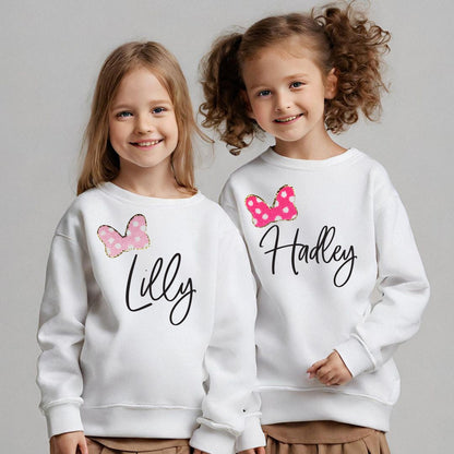 two young girls wearing matching sweatshirts with bows