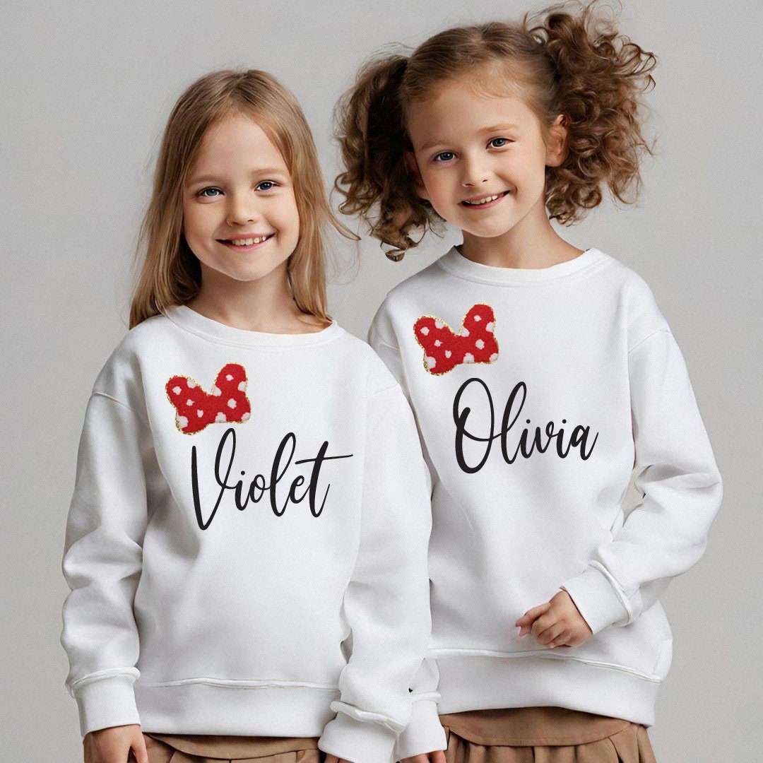 two young girls wearing matching sweatshirts with bows