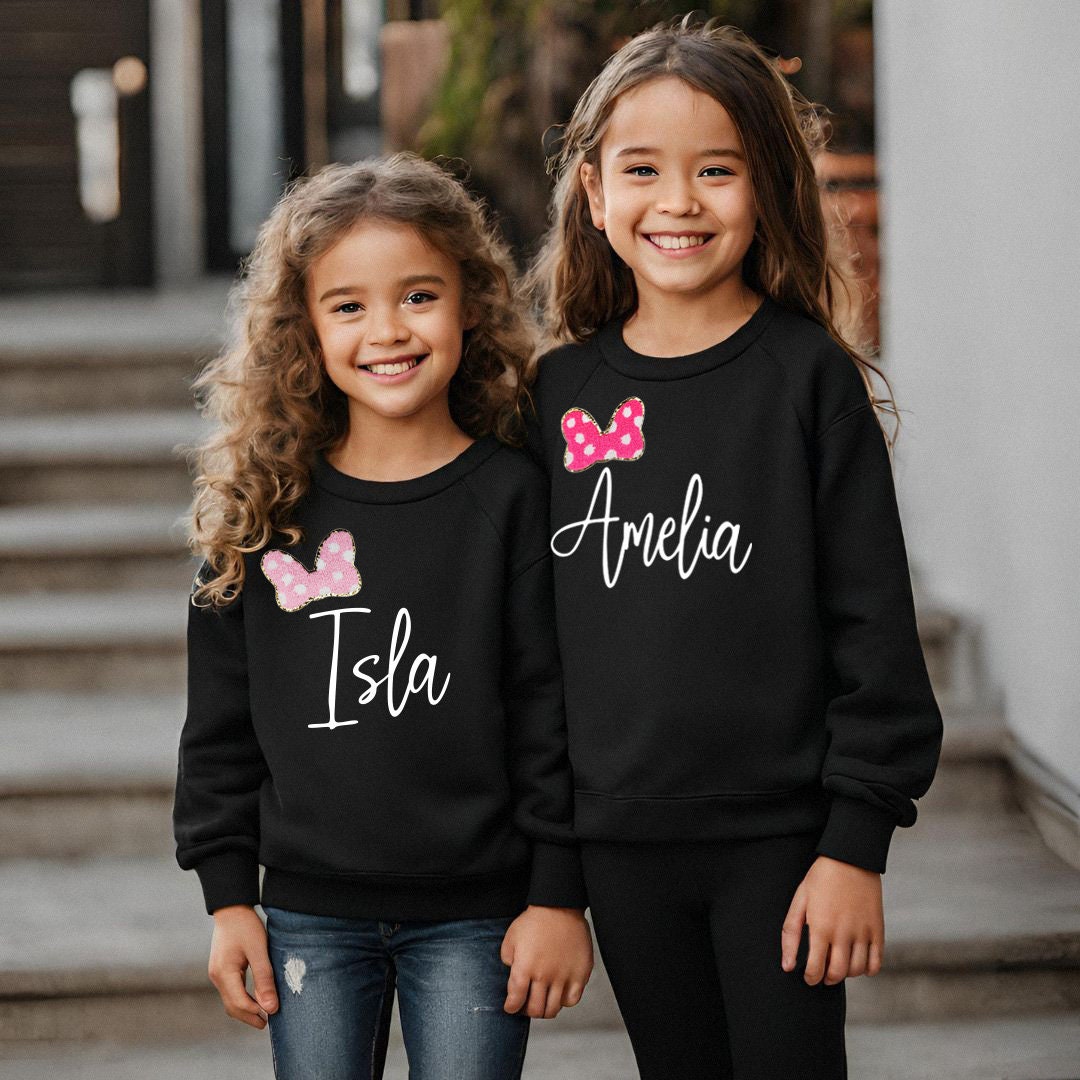 two young girls wearing matching sweatshirts with bows