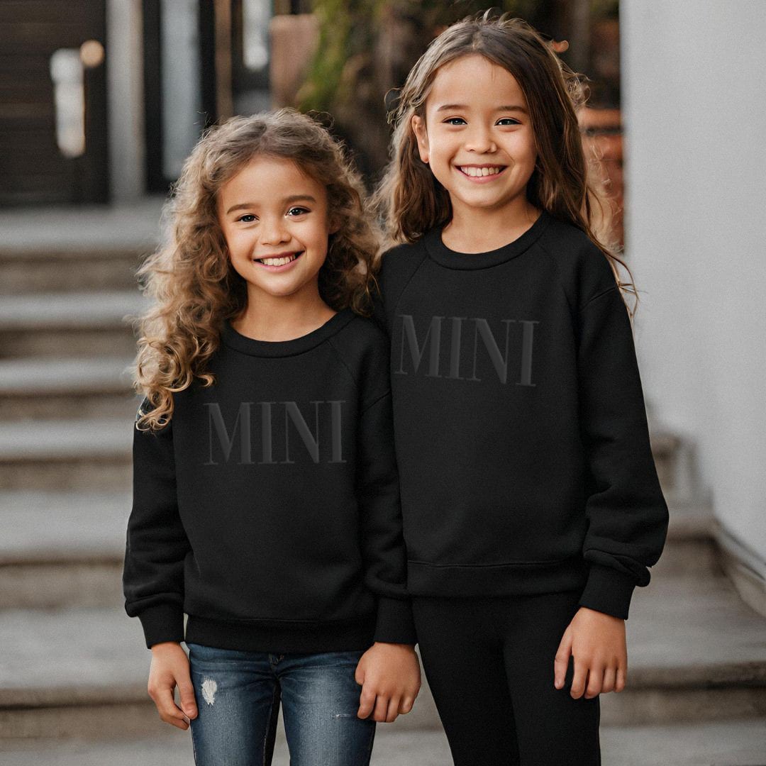 two young girls wearing black sweatshirts with the word mini on them